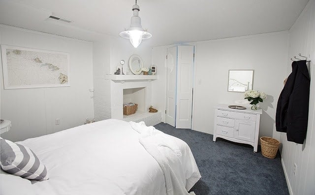 一间白色的卧室，上面有蓝色地毯，并在架子上周围有各种小针织诀窍。