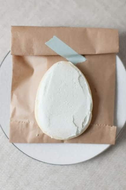 鸡蛋形状的白色糖霜饼干，放在棕色纸袋上。gydF4y2Ba