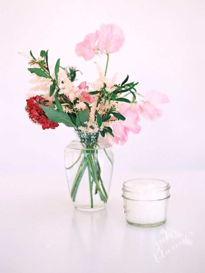 在桌子上的花瓶中，一小束花朵在桌子上，旁边有一罐糖磨砂膏。