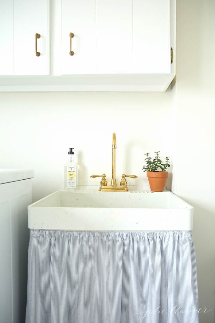洗衣房水槽，带有金水龙头和盆栽植物。