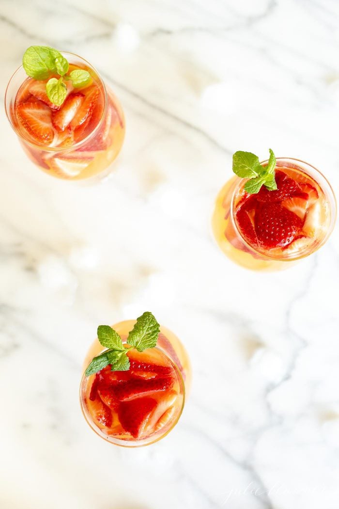 3杯桃子桑格利亚汽酒，上面放着草莓，上面饰有薄荷糖GydF4y2Ba