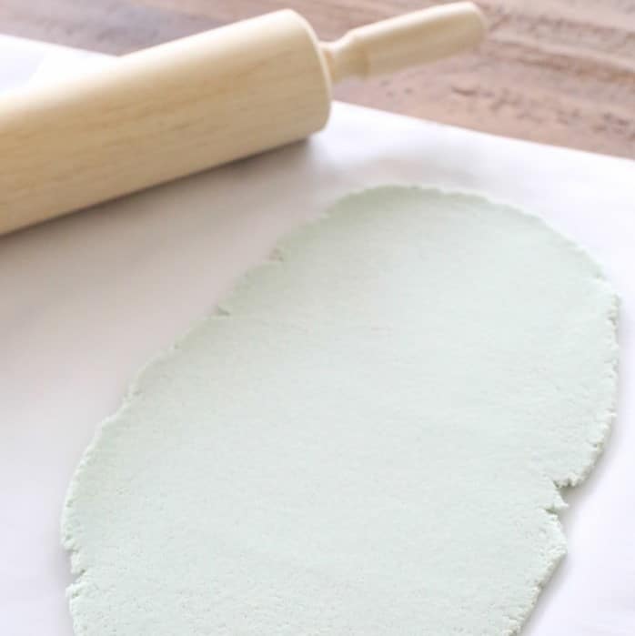 把彩色盐面团擀成绿色面团放在羊皮纸上，木擀面杖放在一边。