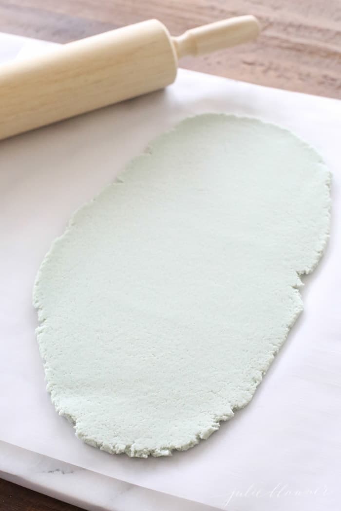 把彩色盐面团擀成绿色面团放在羊皮纸上，木擀面杖放在一边。