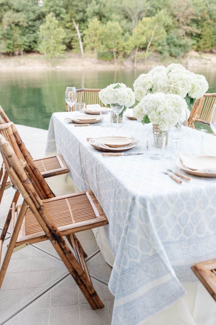 一组在户外餐桌白色的鲜花和一个蓝色和白色的桌布,水在后台。