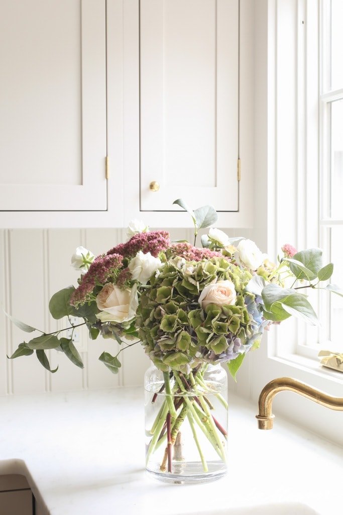在白色厨房窗户旁边的玻璃花瓶中的一个简单的秋天花卉布置。