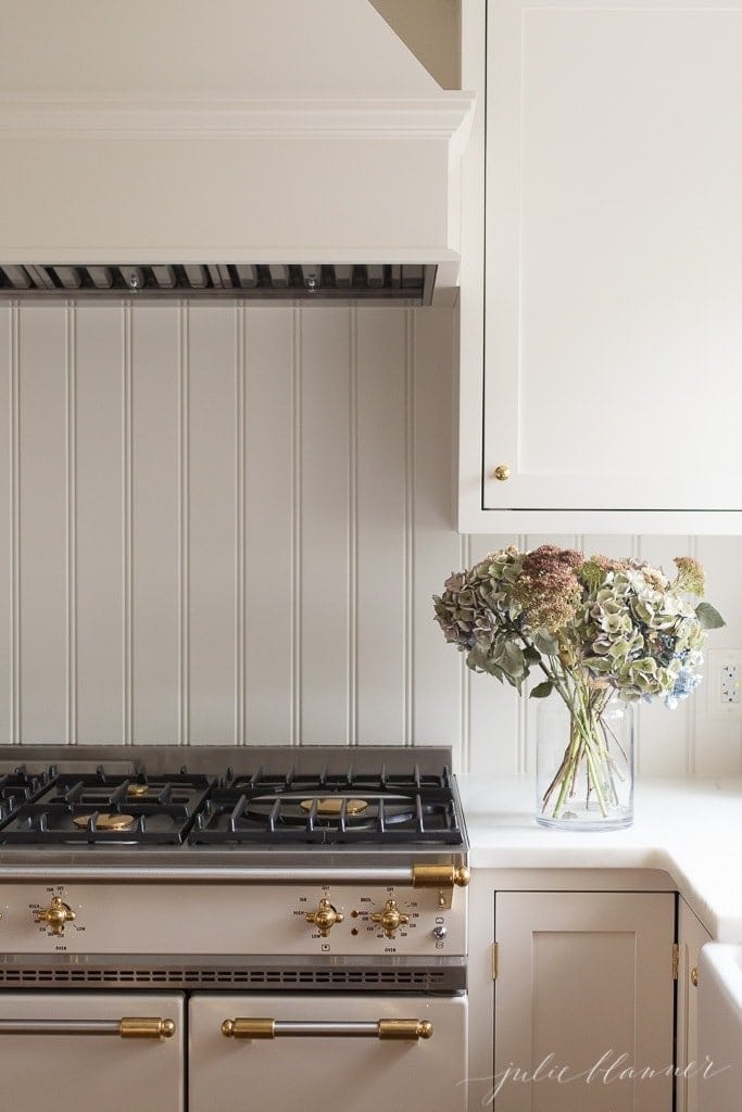 一个白色的厨房，带有珠板后挡板，柜台上的花瓶。