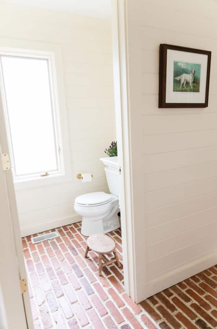 一间带水平雪松镶板和砖地板的客人浴室。