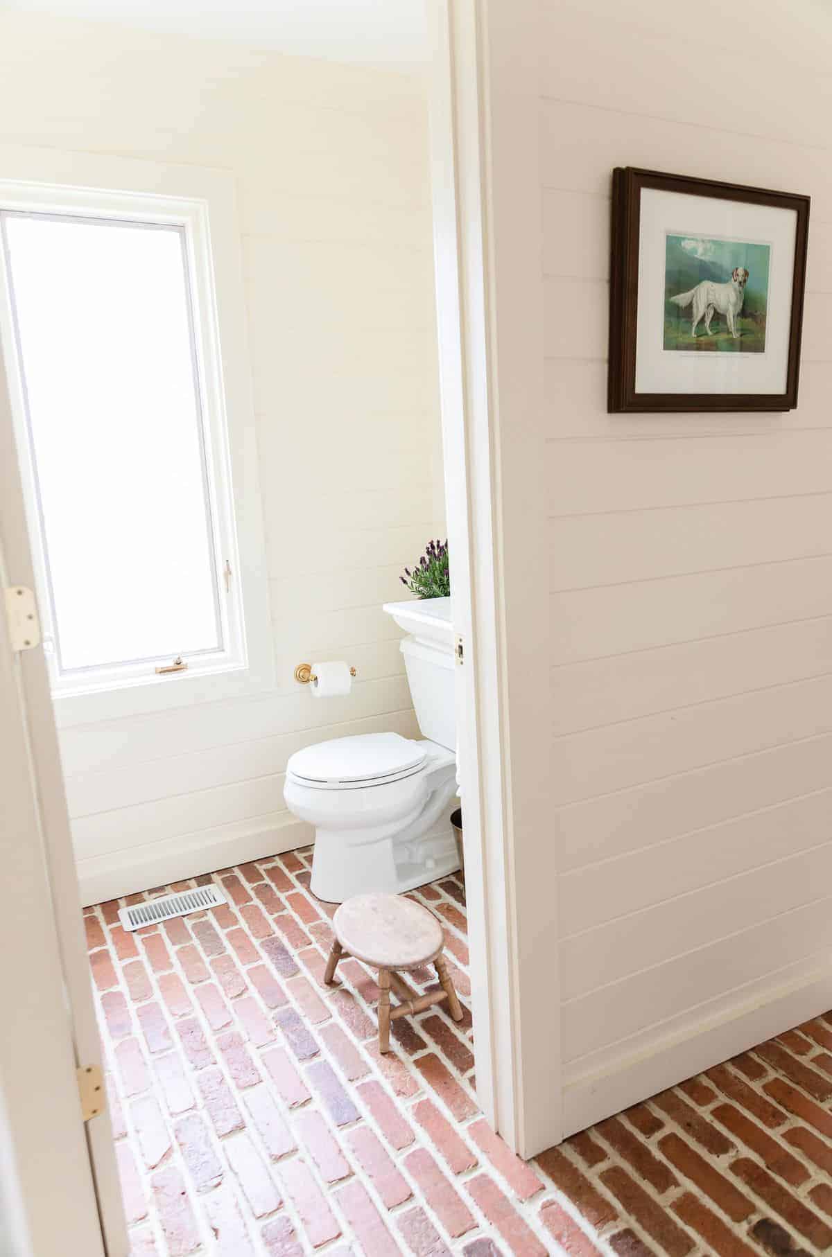 一间客用浴室，铺着水平的雪松镶板和砖地板，厕所后面放着一盆薰衣草木。