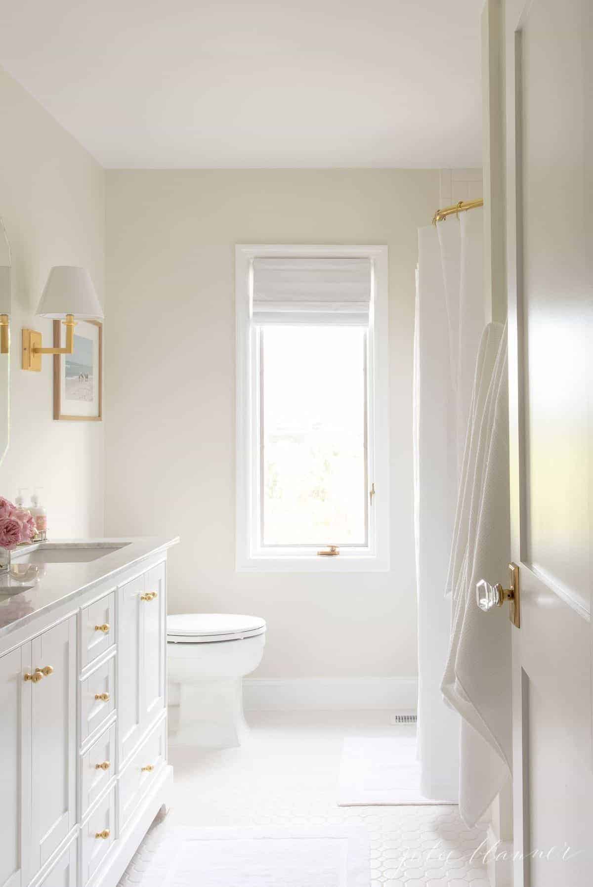 看一间白色的浴室，门上略微ajar。金色的金色和粉红色的花朵上。#spabath