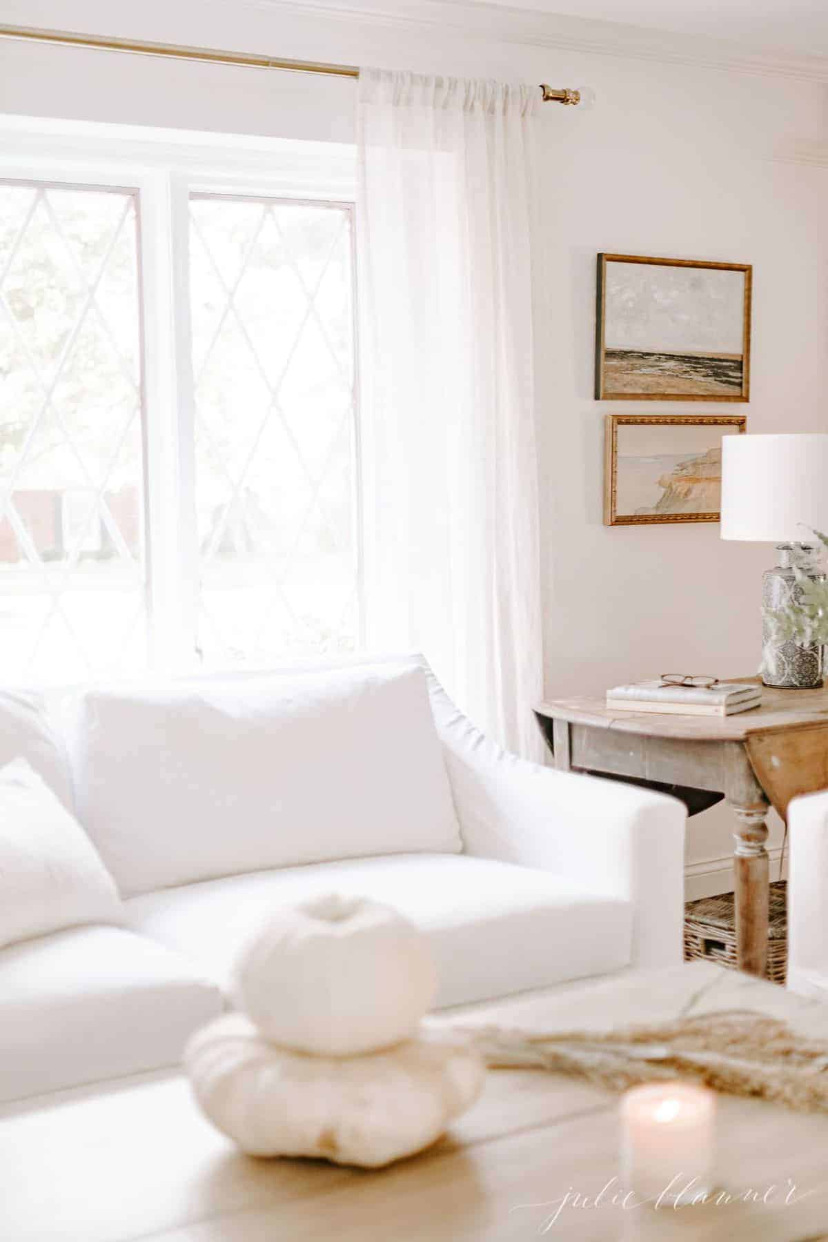 客厅里有白色沙发，后面有窗户。前景中咖啡桌上的白色南瓜。# falllivingroom