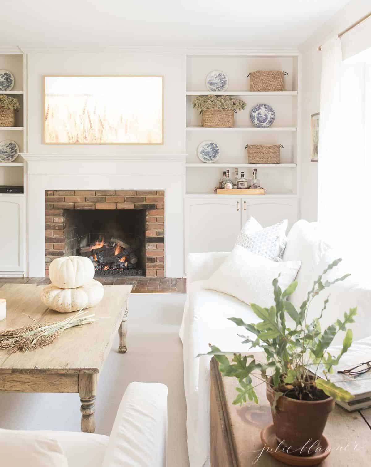 向后拉的视角是为秋季装饰的客厅，咖啡桌上摆放着南瓜和小麦，背景是燃烧的壁炉。# fallharvestdecor