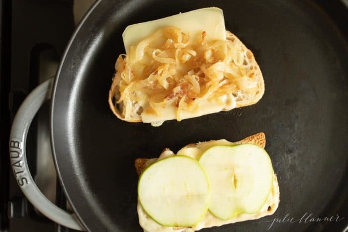 铸铁煎锅，上面放两片面包片，奶酪片，苹果和焦糖洋葱。gydF4y2Ba
