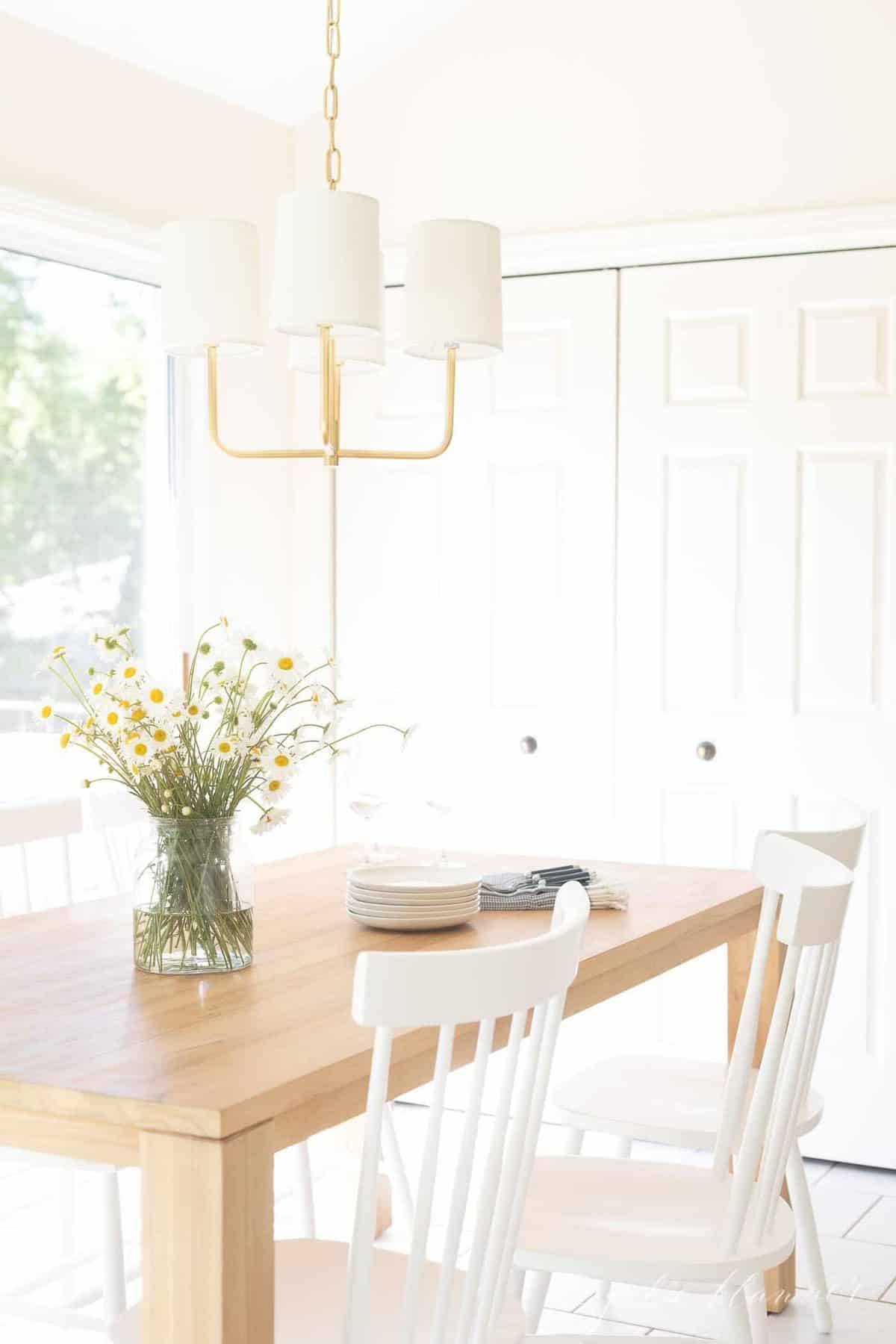 一个明亮的白色厨房，带有木桌和黄铜吊灯。