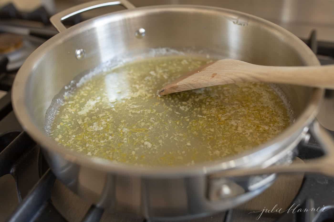 炉子上的一个银锅，融化的黄油和大蒜用木制刮刀搅拌。GydF4y2Ba