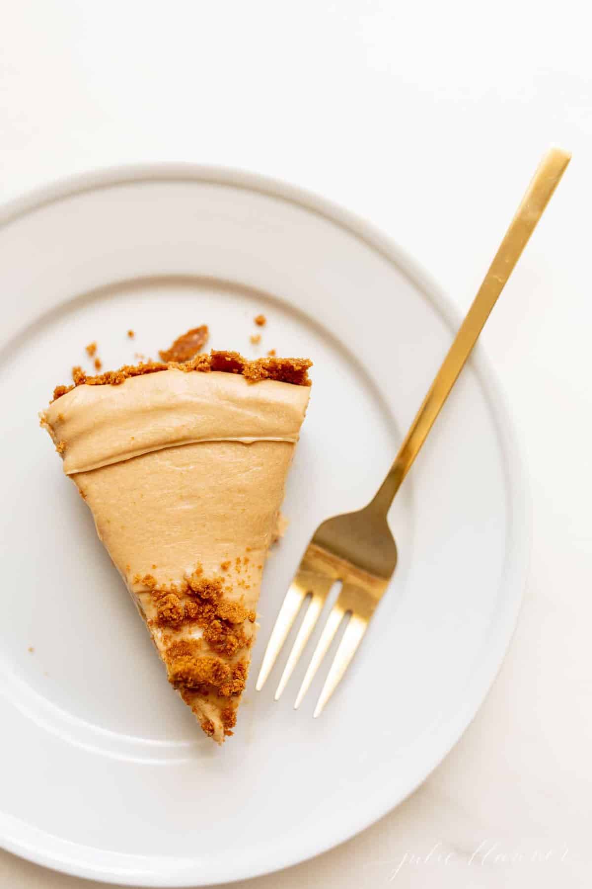 一个白色的表面用一个白色的盘子放着一片曲奇黄油芝士蛋糕，金色的叉子放在一边。gydF4y2Ba