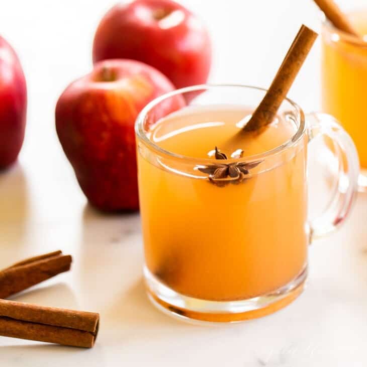 一个大理石表面，上面有透明的杯子，里面装满了自制的苹果酒，整个苹果和肉桂粘在侧面。