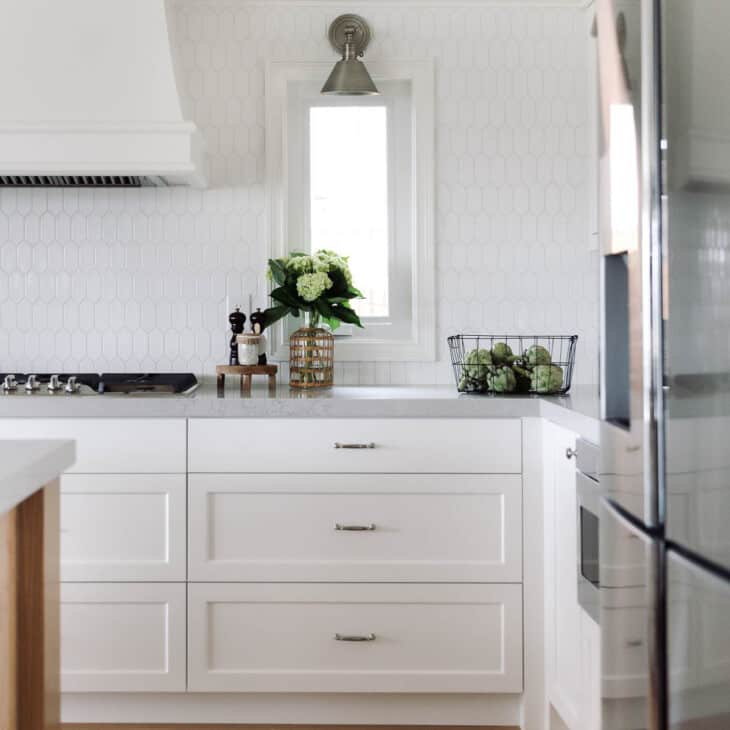 有白色六边形瓷砖后挡板和白色橱柜的厨房。