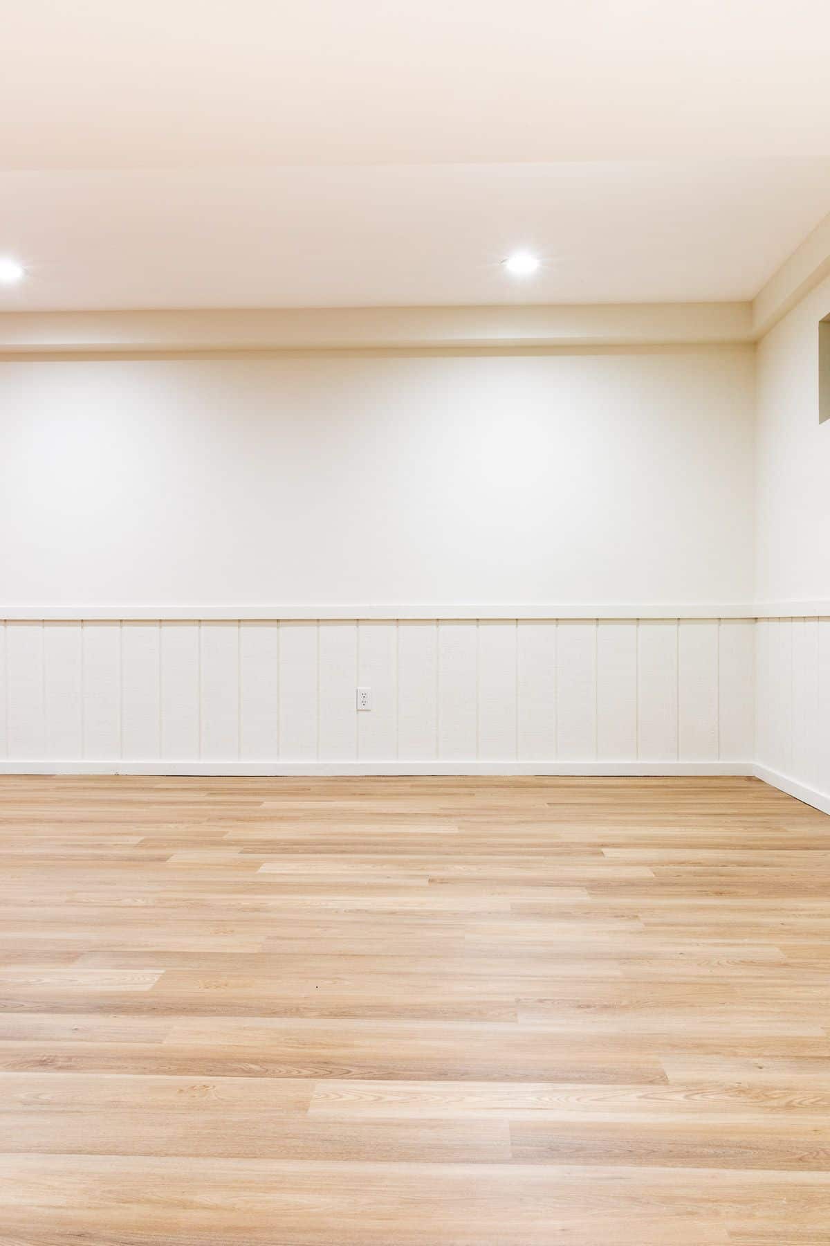 一个空的地下室，白色的墙壁和中色调的乙烯基木板地板。